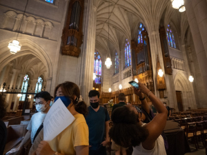 A group of students on a tour of Duke Chapel. One of them points a phone at the ceiling.