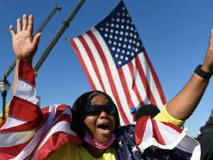 A Black woman celebrates Biden's win with an American flag in the background
