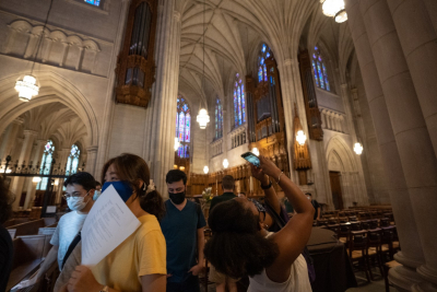 A group of students on a tour of Duke Chapel. One of them points a phone at the ceiling.